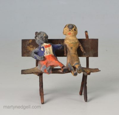 Toy soft metal golly and doll on a bench, circa 1900