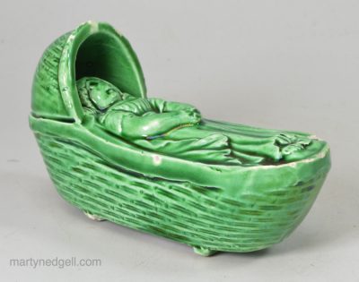 Green glazed creamware pottery toy cradle and sleeping child, circa 1820