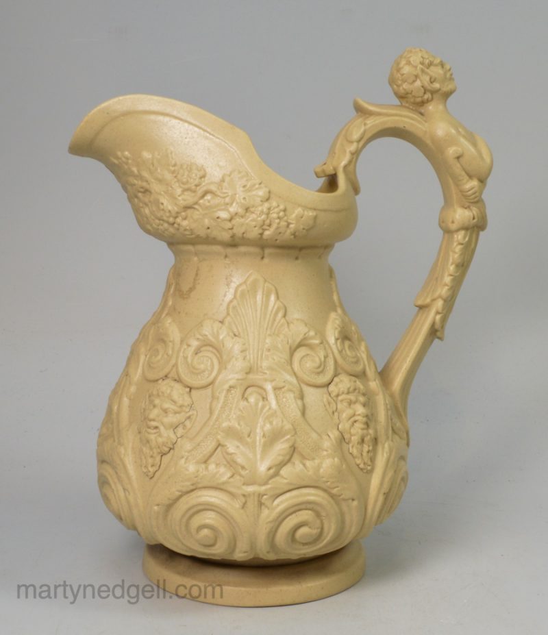 Drab stoneware jug moulded with Bacchanalian faces and Pan for a handle, circa 1850, probably Ridgways Pottery Staffordshire