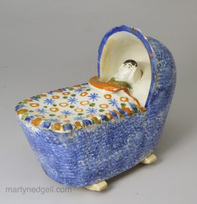 Prattware pottery toy baby in a cradle, circa 1820, probably Bovey Tracey Pottery