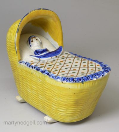 Prattware pottery toy cradle and baby, circa 1800, possibly Bovey Tracey