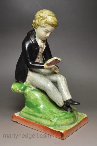 Staffordshire pearlware pottery figure of a boy reading decorated with overglaze enamels, circa 1830