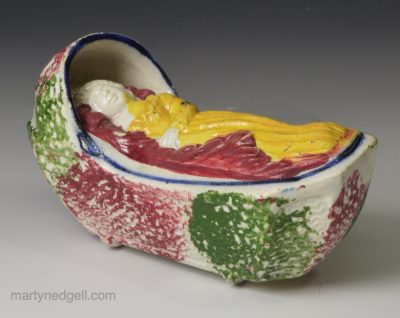Pealware pottery toy cradle and child with sponged decoration, circa 1830