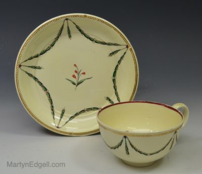 Creamware pottery cup and saucer decorated with enamels over the glaze, circa 1800